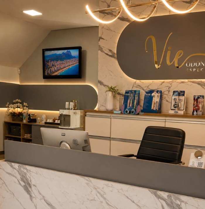 Recepção da Vie Odontologia, com balcão de mármore e o logo em dourado na parede